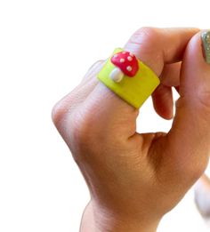 a hand holding a yellow and green ring with a red mushroom on it's side