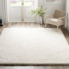 a large white rug in the corner of a room with a chair and potted plant