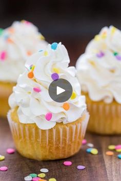 three cupcakes with white frosting and sprinkles on a table