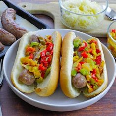 two hot dogs on buns with peppers, onions and sauerkraut in the background