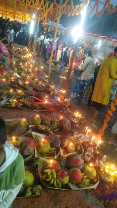 many people are standing around with candles and fruit on the ground in front of them