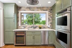 a kitchen with green cabinets and stainless steel appliances in front of a window that looks out onto the trees