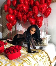 a woman laying on top of a bed next to red balloons