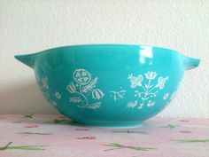 a blue bowl with white designs on it sitting on a tablecloth covered table next to a wall