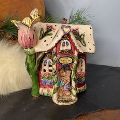 a ceramic figurine of a house with flowers on the table next to it