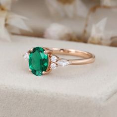 an emerald and diamond ring sitting on top of a white box with flowers in the background