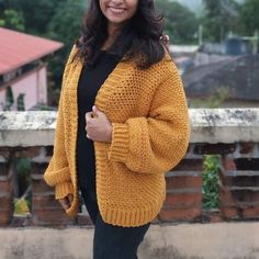 a woman wearing a yellow cardigan standing on top of a roof with her hands in her pockets