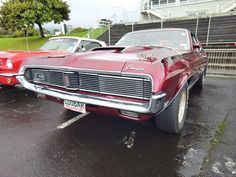 two classic cars parked in a parking lot next to each other on a rainy day