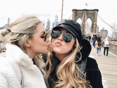 two women kissing each other in front of the brooklyn bridge with people walking on it