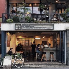 people sitting at tables in front of a building with plants growing on the balconys