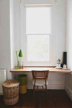 a room with a desk, chair and lamp on it in front of a window