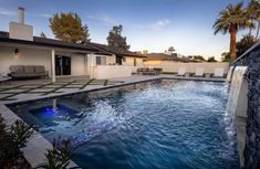 an outdoor swimming pool with waterfall and lounge chairs in the background at sunset or dawn