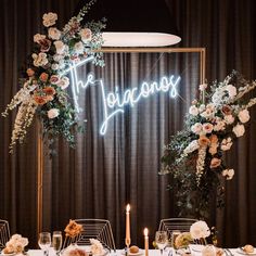 the neon sign is lit up above an elegant dinner table set with flowers and candles