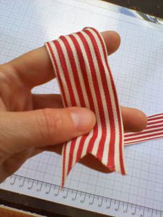 a person is holding a red and white striped ribbon on a piece of paper with a ruler in the background