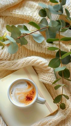 a cup of cappuccino on top of a book next to some leaves