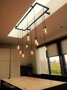 a wooden table sitting in front of a window with light bulbs hanging from the ceiling