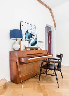 a piano sitting in the corner of a living room next to a chair and lamp