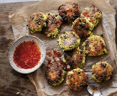 several crab cakes with ketchup on a piece of parchment paper next to a bowl of sauce