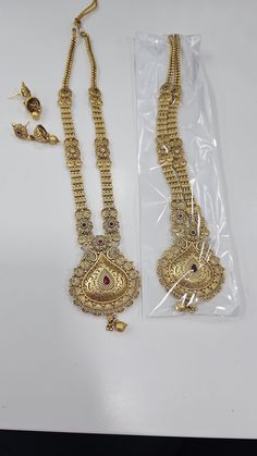 Long gold necklace set. It's a simple elegant set with details of design. The design mixed with mesh with red stone work on the pendant makes it gorgeous. The pendant is finished with gold bead on it. The side chains have beautiful small flower and design chain. There is dori on the back to adjust the length. Comes with super cute jhumkis. Looks like real gold set.  P. S: non returnable product.Please ask any question if you have related to this product before purchasing as returns for size, col Gold Temple Jewelry Long Necklace For Festive Occasions, Festive Gold Jewelry Set With Stone Work, Festive Gold Temple Jewelry Long Necklace, Traditional Gold Long Necklace For Festive Occasion, Heavy Gold Long Bridal Necklace, Festive Formal Necklace With Latkans, Gold Long Bridal Necklace, Heavy Gold Kundan Long Necklace, Gold Long Necklace For Weddings, Temple Style