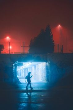 a person walking through a tunnel with street lights in the background on a foggy night