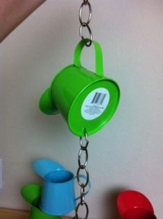 a green watering can hanging from a chain with other toys in the corner behind it