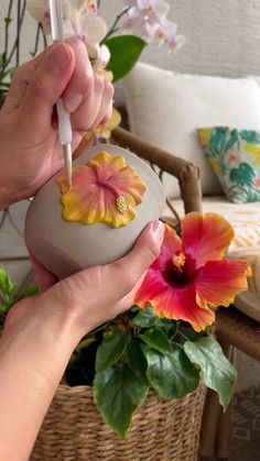 a person holding a flower in their hand near a basket with flowers on the table