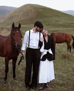 a man and woman standing next to each other with horses in the background