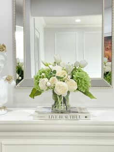 a vase filled with white flowers sitting on top of a table next to a mirror