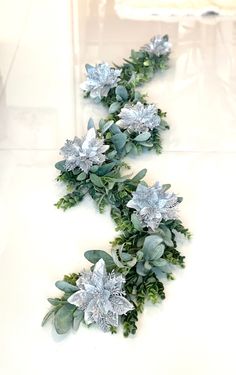 some silver flowers and green leaves on a white table