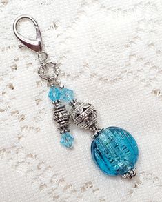 a blue glass beaded keychain hanging from a metal hook on a white fabric