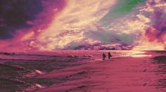 two people walking on the beach at sunset with colorful clouds in the sky above them