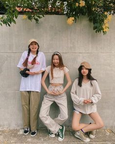 three young people standing next to each other in front of a cement wall with yellow flowers