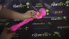 a person holding a pink toy in front of a black backdrop with the word tomy written on it