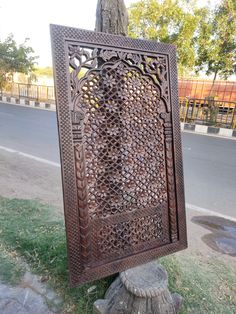 an intricately carved metal sign sitting on the side of a road next to a tree