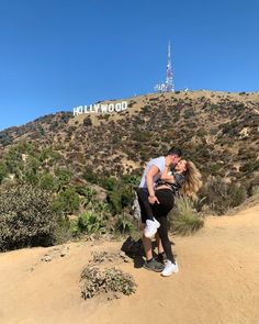 a man and woman kissing in front of the hollywood sign on top of a hill