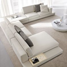 a large white sectional sofa sitting on top of a carpeted floor next to a window