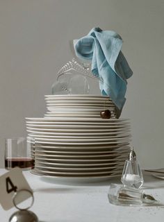 a stack of white plates sitting on top of a table next to glasses and silverware