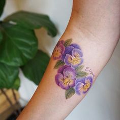 a woman's arm with purple and yellow flowers tattooed on the left side of her arm