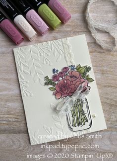 some crayons and markers are next to a card that has flowers in a mason jar