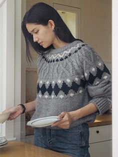 a woman standing in front of a kitchen counter holding a plate and looking down at it