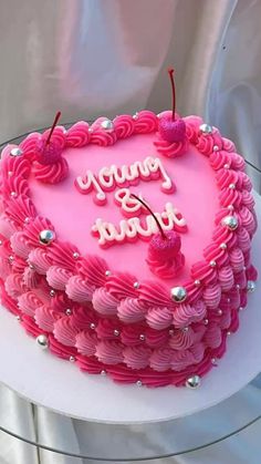 a pink heart shaped cake with the words happy birthday written on it and two cherries