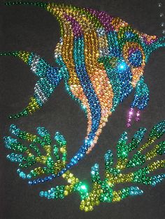 a colorful fish made out of beads on a black surface with green and blue leaves