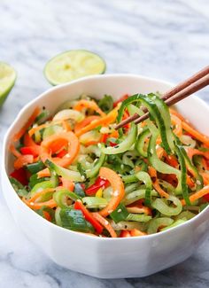 a white bowl filled with veggies and chopsticks next to sliced cucumbers