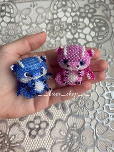 two small stuffed animals sitting on top of someone's hand in front of a lace tablecloth