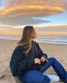 a woman sitting on the beach with her eyes closed and looking up at the sky