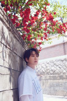 a young man leaning against a wall with red flowers growing on it's side