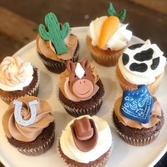 cupcakes are decorated with farm animals and cactus decorations on a white platter