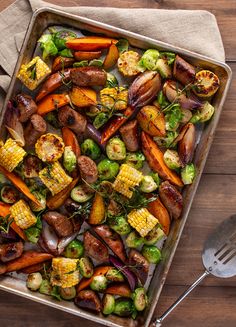 a pan filled with vegetables and meat on top of a wooden table next to a fork