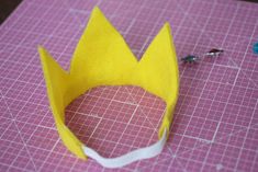 a yellow paper crown sitting on top of a cutting board next to scissors and thread