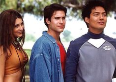 three young people standing next to each other in front of a tree and grass area